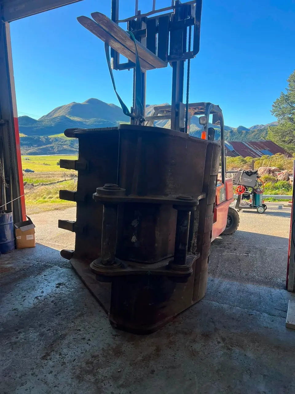 Large painted bucket carried on a forklift outside the workshop