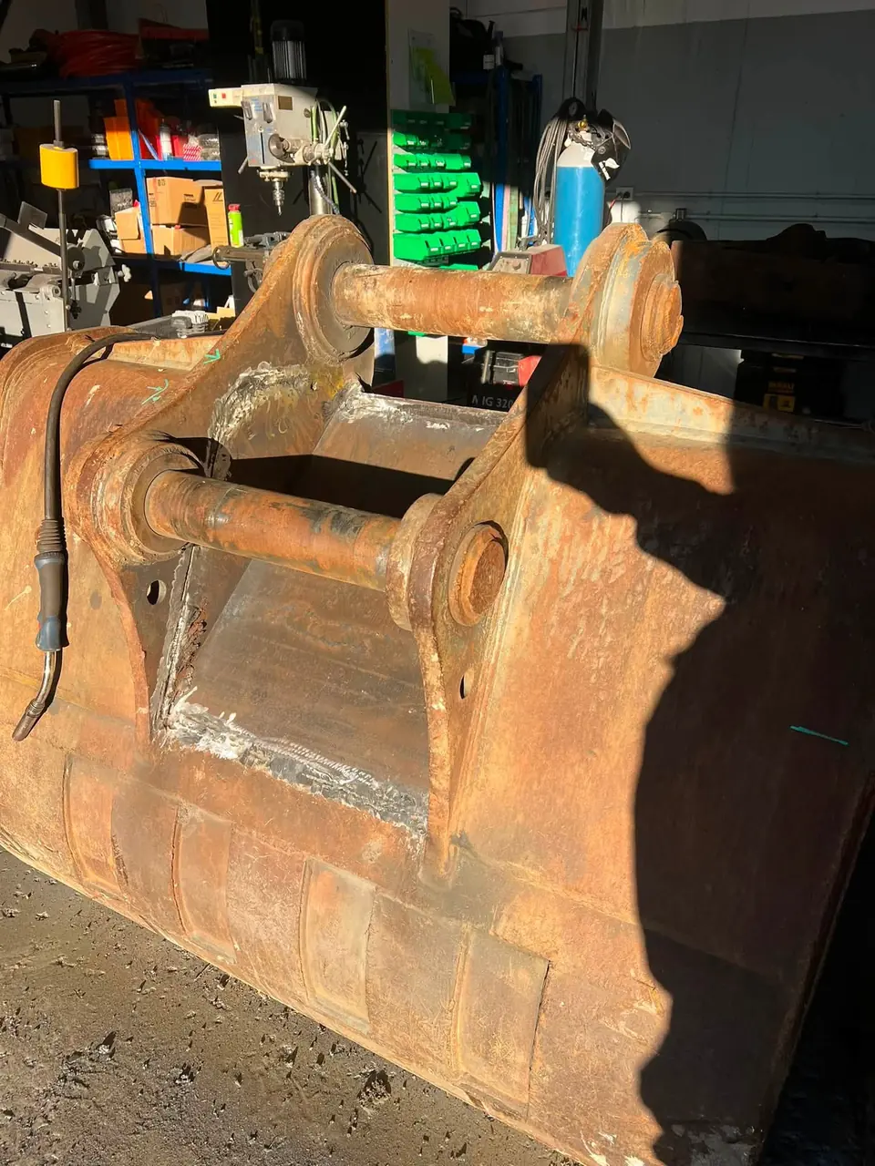 Rusted excavator bucket sitting on the concrete outside the workshop